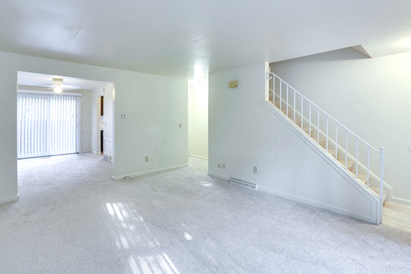 A spacious room with a staircase and a window with blinds.