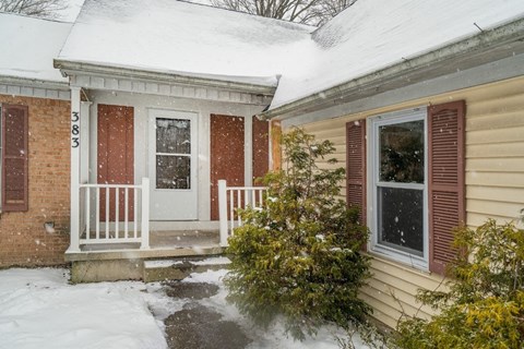 A house with a white door and red shutters is covered in snow.