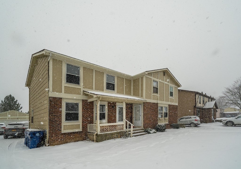 A house with a brown and beige exterior is surrounded by snow.