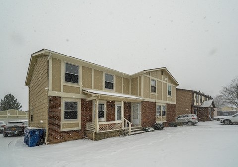 A house with a brown and beige exterior is surrounded by snow.