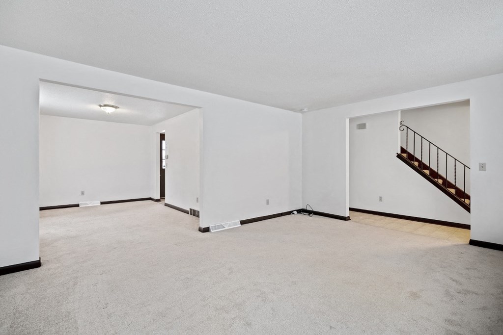 A spacious empty room with a staircase on the right side.