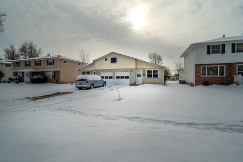 A car is parked in front of a house on a snowy street.