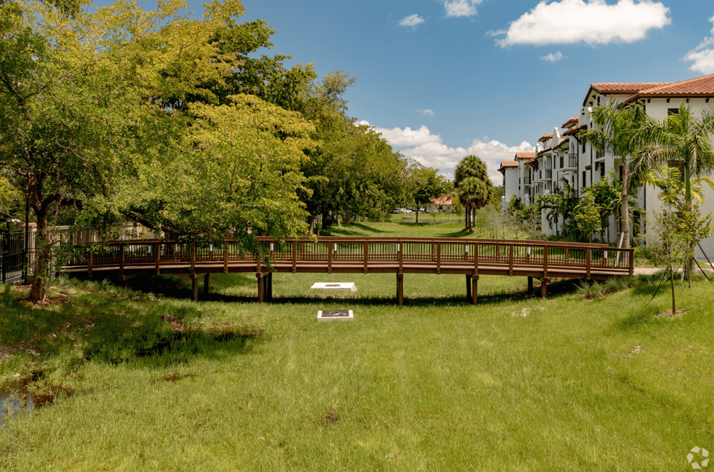 a bridge over a grassy area with trees and buildings in the background
