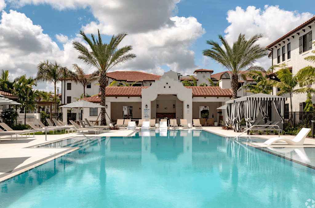 a resort style swimming pool with white lounge chairs and palm trees
