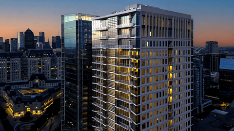 A modern glass building stands tall among other buildings in a cityscape at dusk.