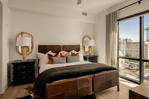 A bedroom with a large bed, two lamps, and a view of the city.
