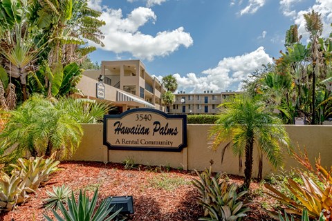 A sign for Hawaiian Palms A Rental Community is in front of a building.