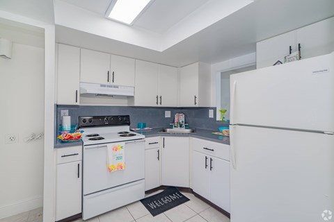 A kitchen with white appliances and a black mat on the floor.