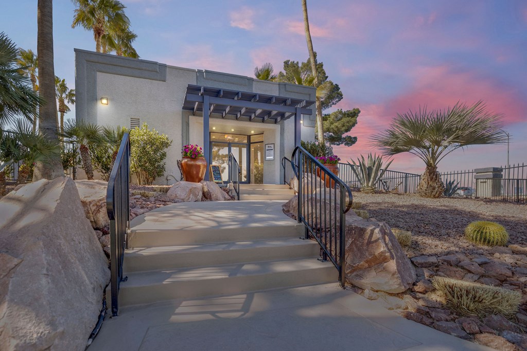 a stairway leading up to a house with a porch and rocks and a sunset