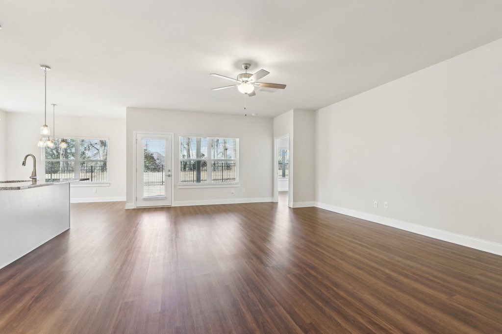 Living room with ample amount of space with wood floors and a ceiling fan.