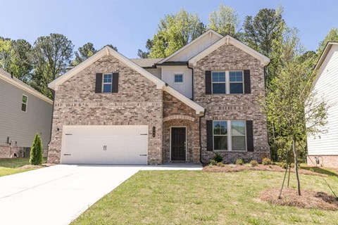A two-story house with a garage is surrounded by a well-maintained lawn and trees.