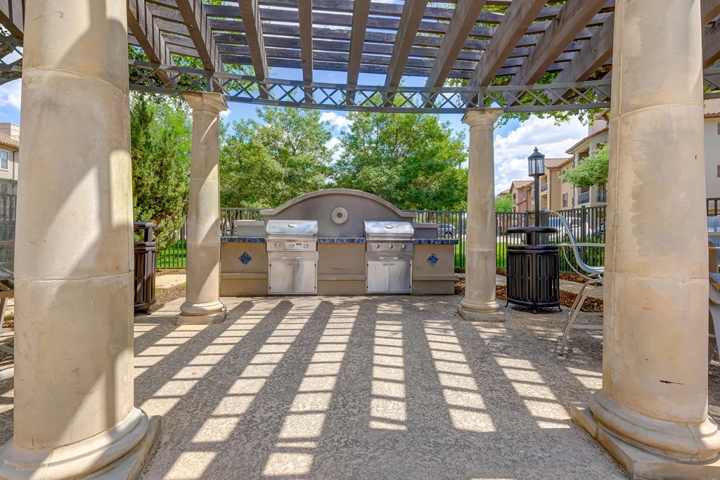 an outdoor kitchen with two bbq grills and a pergola
