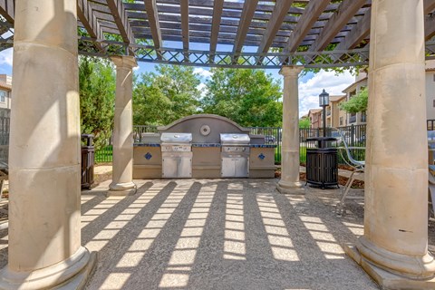 an outdoor kitchen with two bbq grills and a pergola