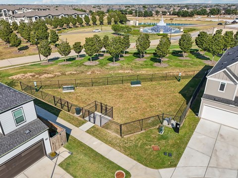 an aerial view of a fenced in dog park with a pool in the background