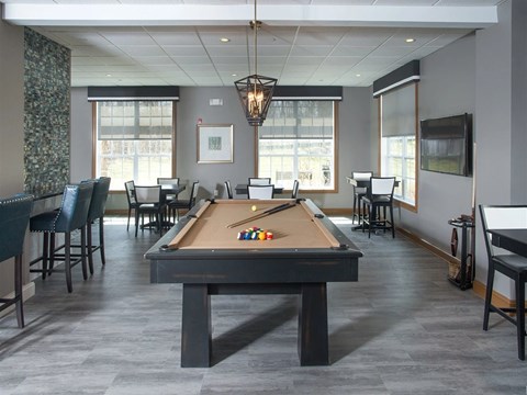 A pool table is in the middle of a room with chairs and a television.