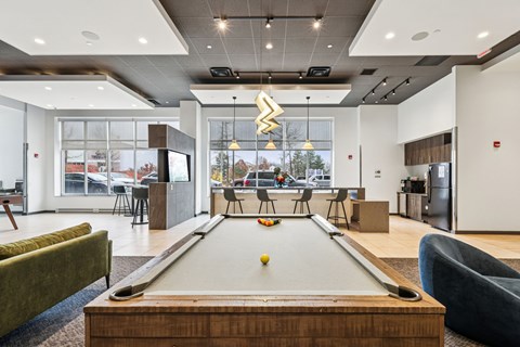 A pool table is in the middle of a room with a green couch and a blue chair.