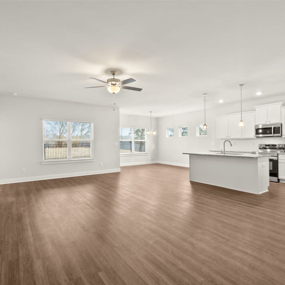 an empty living room with a kitchen and a ceiling fan
