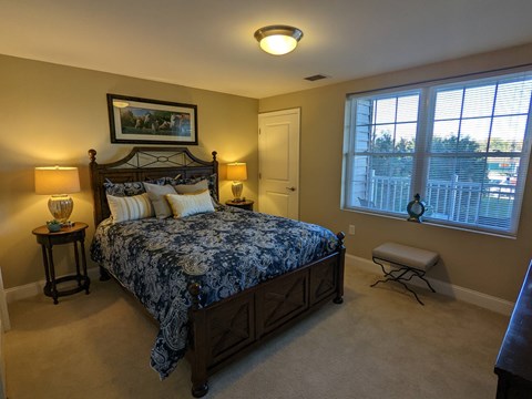 A bedroom with a large bed and a window overlooking a fence.