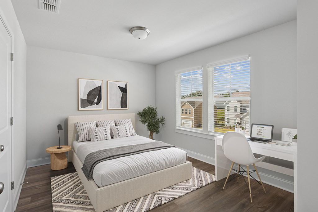 Secondary bedroom with queen bed, large sunlit window, and workspace with desk and chair.