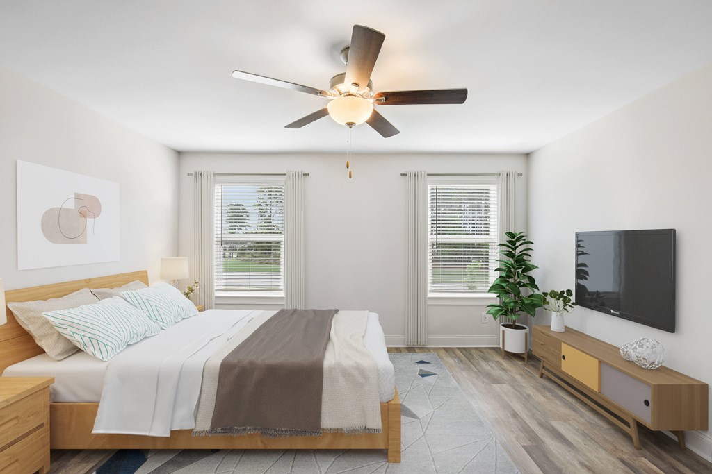 Another perspective view of the serene primary suite, showcasing a modern ceiling fan, sleek entertainment, and sunlit window views.