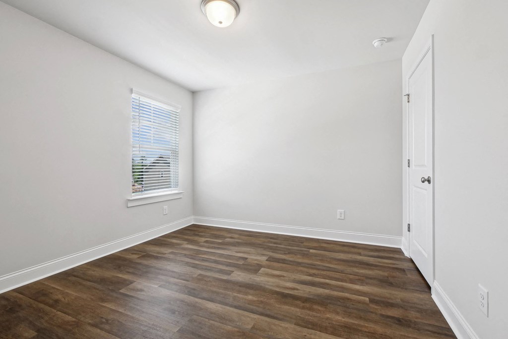 an empty room with white walls and wood flooring and a window