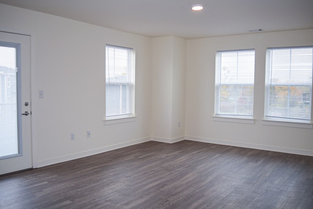 an empty living room with wood floors and three windows