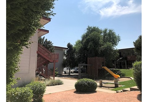 A playground with a yellow slide is surrounded by green bushes and trees.