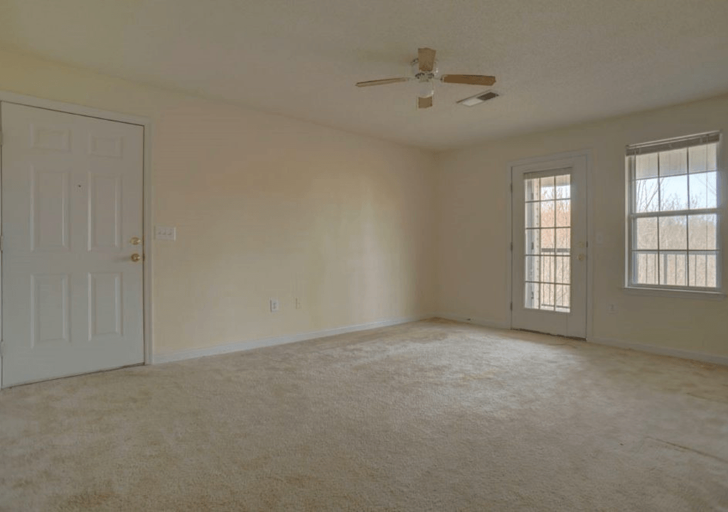 an empty living room with a ceiling fan and a door