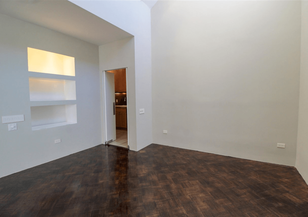 A room with a wooden floor and a white wall with a shelf and a door.