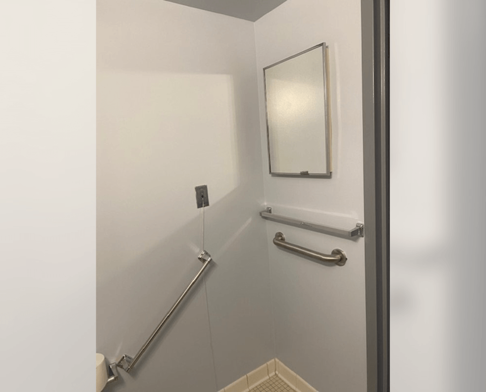 a white bathroom with two grab bars and a mirror