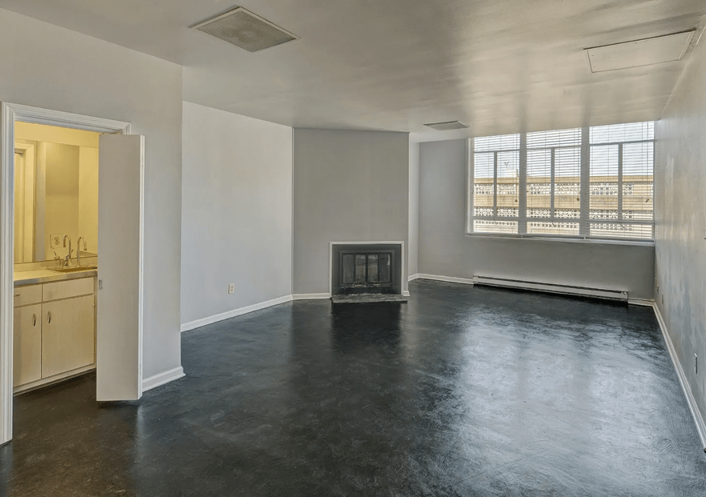 A large empty room with a fireplace and a kitchen area.