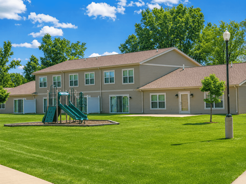 A playground with a green slide is in front of a building.