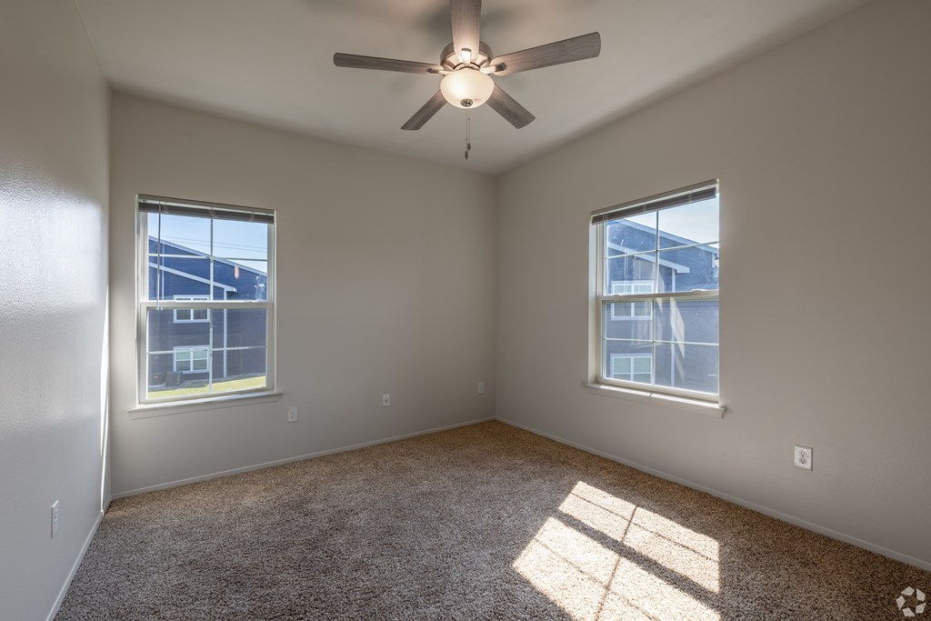 A room with a ceiling fan and two windows.