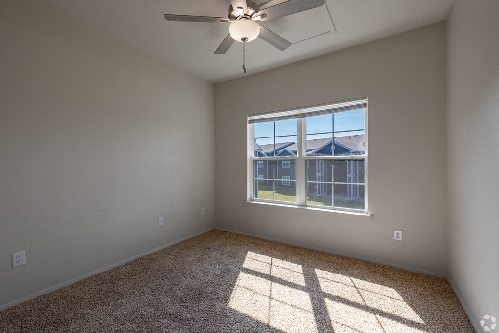 A room with a ceiling fan and a window overlooking a fenced area.