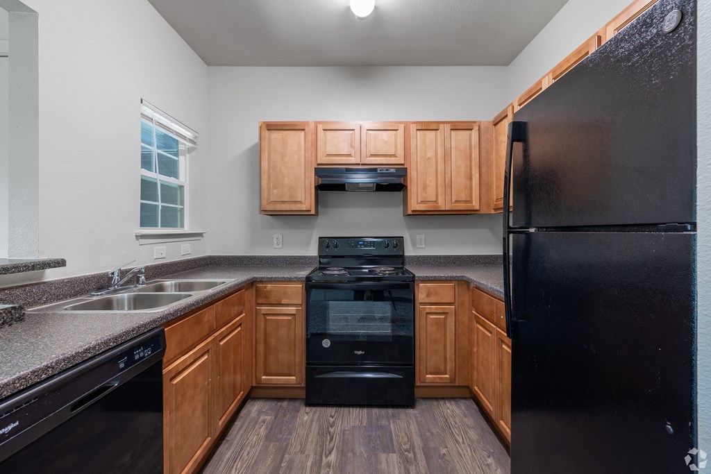 A black refrigerator sits in a kitchen with wooden cabinets.