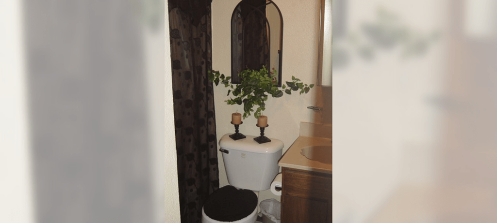 A white toilet with a black seat cover sits next to a sink in a bathroom.
