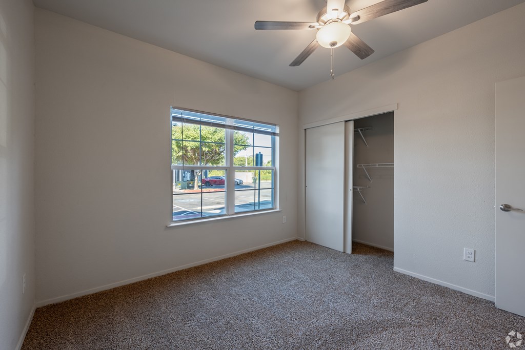 A room with a ceiling fan and a window overlooking a street.