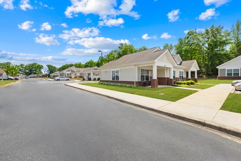 A street view of a residential area with houses on the right and a clear blue sky above.