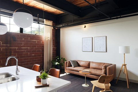 A modern kitchen with a white countertop and brown leather couch.
