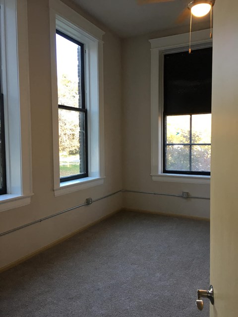 A room with a carpeted floor and two windows.