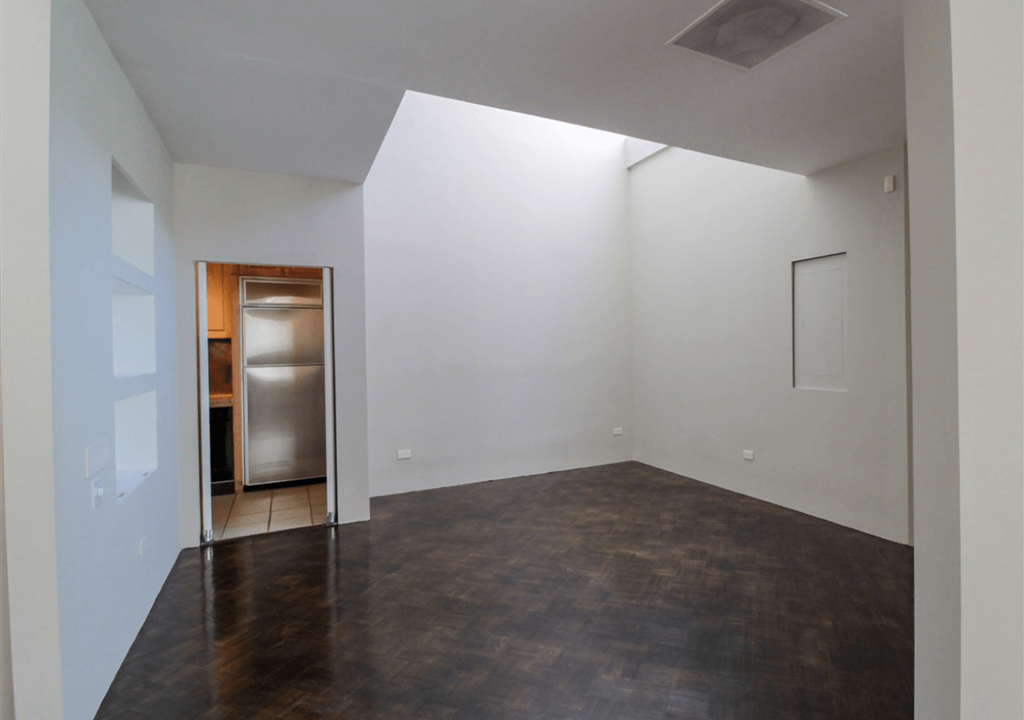 A room with a refrigerator and a doorway leading to another room.