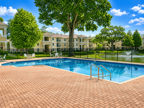 A swimming pool surrounded by a brick patio and a black fence with a building in the background.