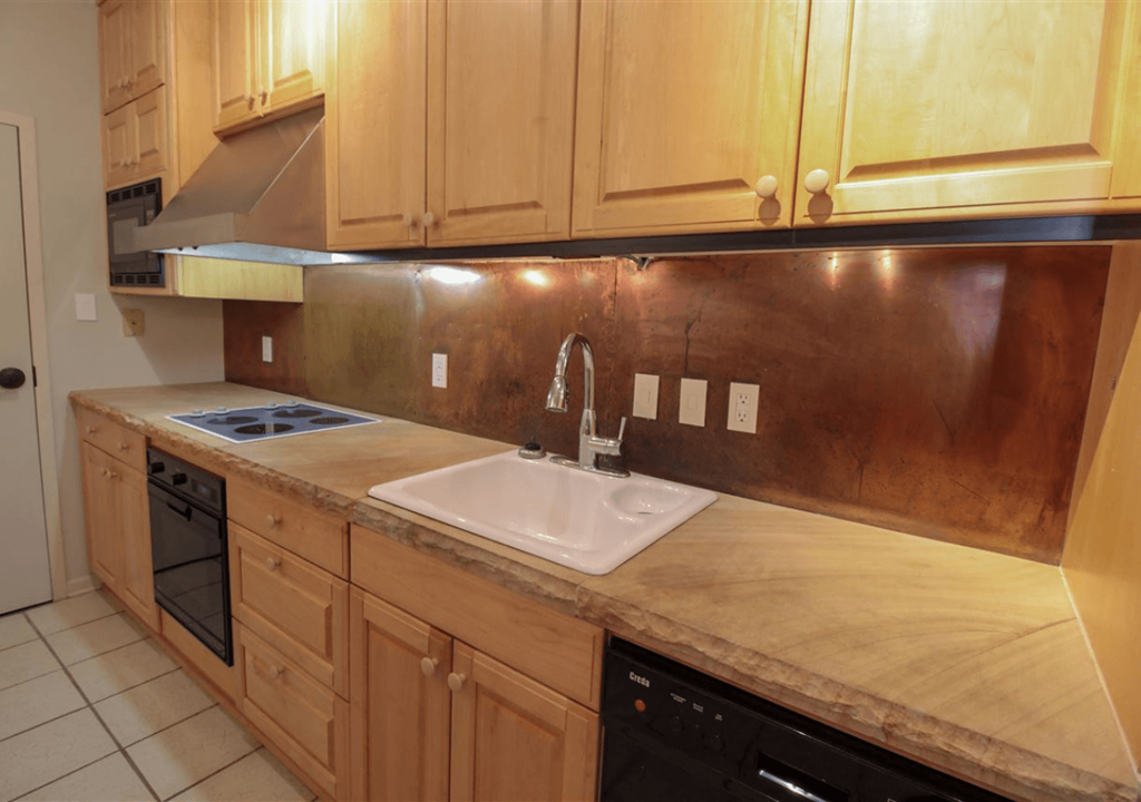 A kitchen with wooden cabinets and a copper backsplash.