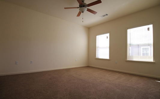 an empty living room with a ceiling fan and two windows