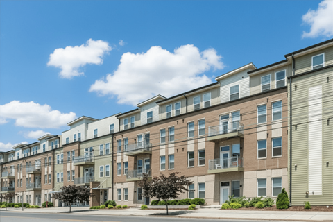 A row of modern apartment buildings with balconies and trees in front.