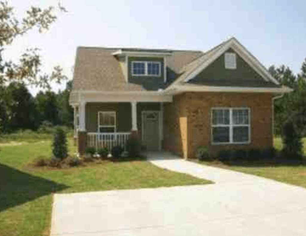 a brown brick house with a green lawn and a white sidewalk
