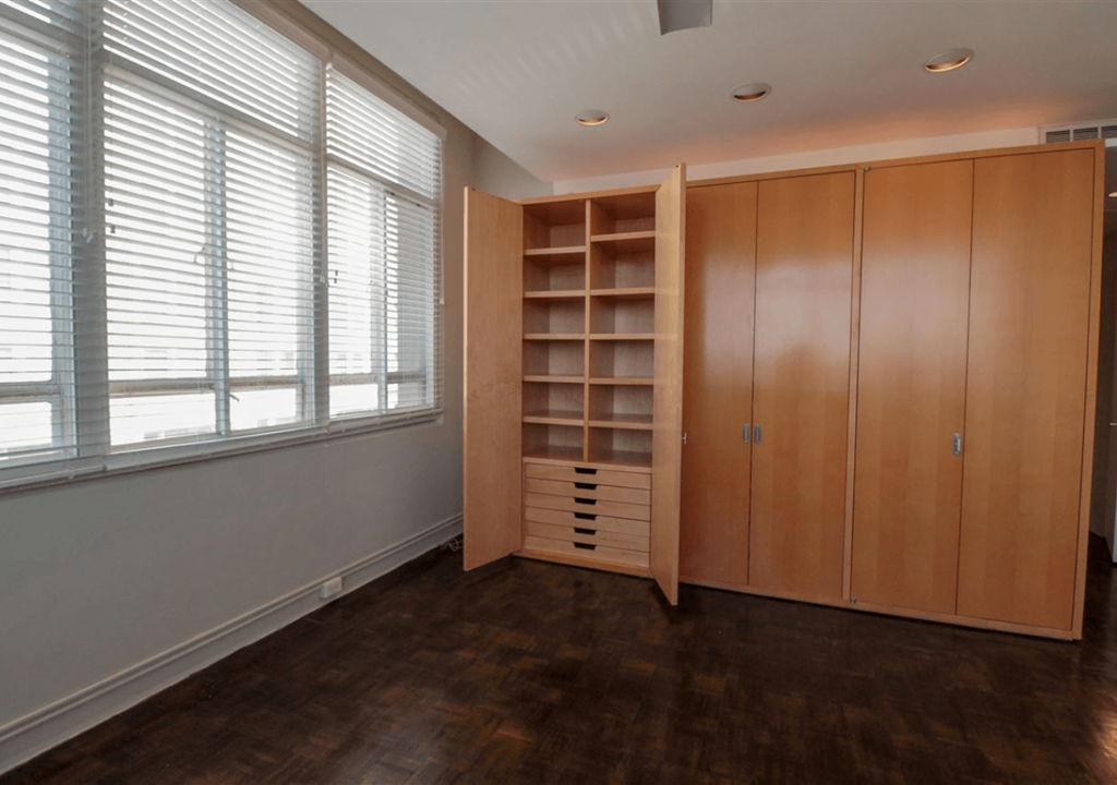 A room with a wooden floor, a large wooden cabinet with shelves, and a window with blinds.