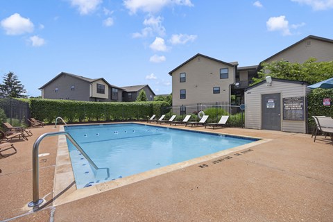 A pool surrounded by chairs and a fence with a building in the background.