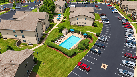 A parking lot with cars and a swimming pool in the middle of a grassy area.