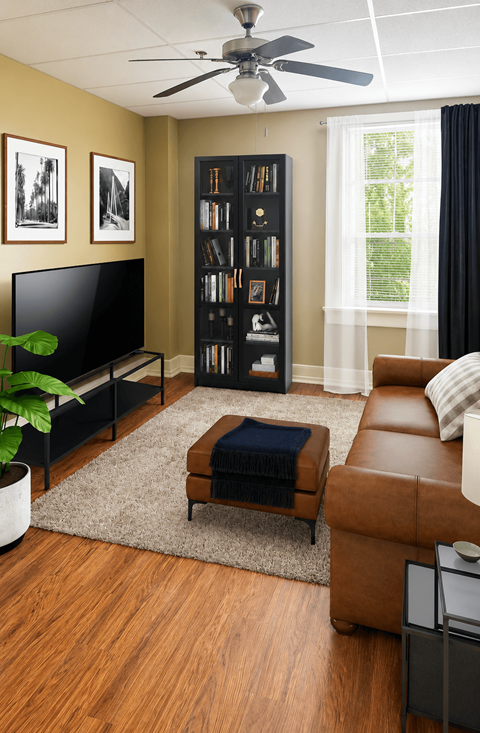 A living room with a brown leather couch, a black television, a brown ottoman, a bookshelf, and a ceiling fan.